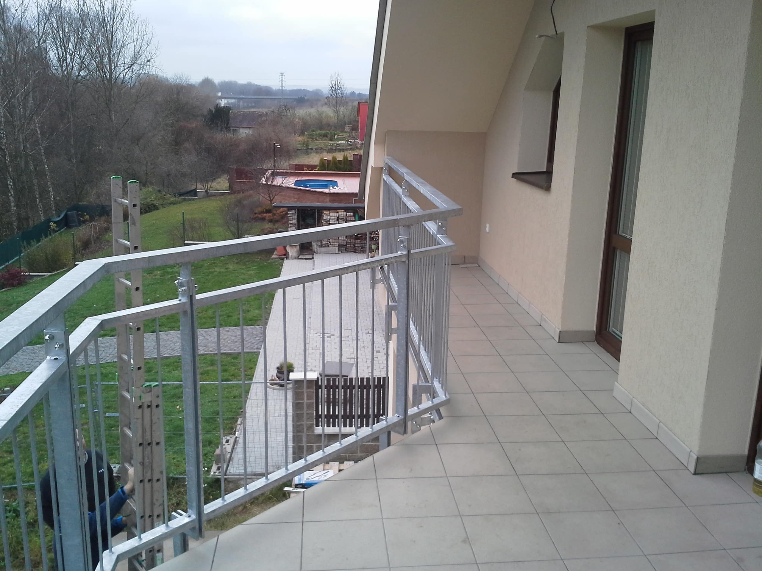 Boční úsek zinkovaného balkónového zábradlí a jeho návaznost na fasádu rodinného domu ve Slaném.