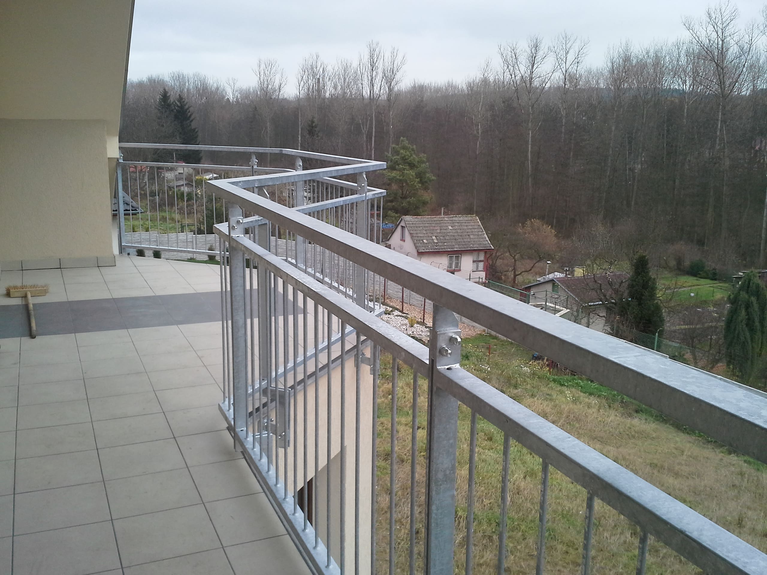 Pohled podél kovového madla na navazující pole atypického balkónového zábradlí ve Slaném.