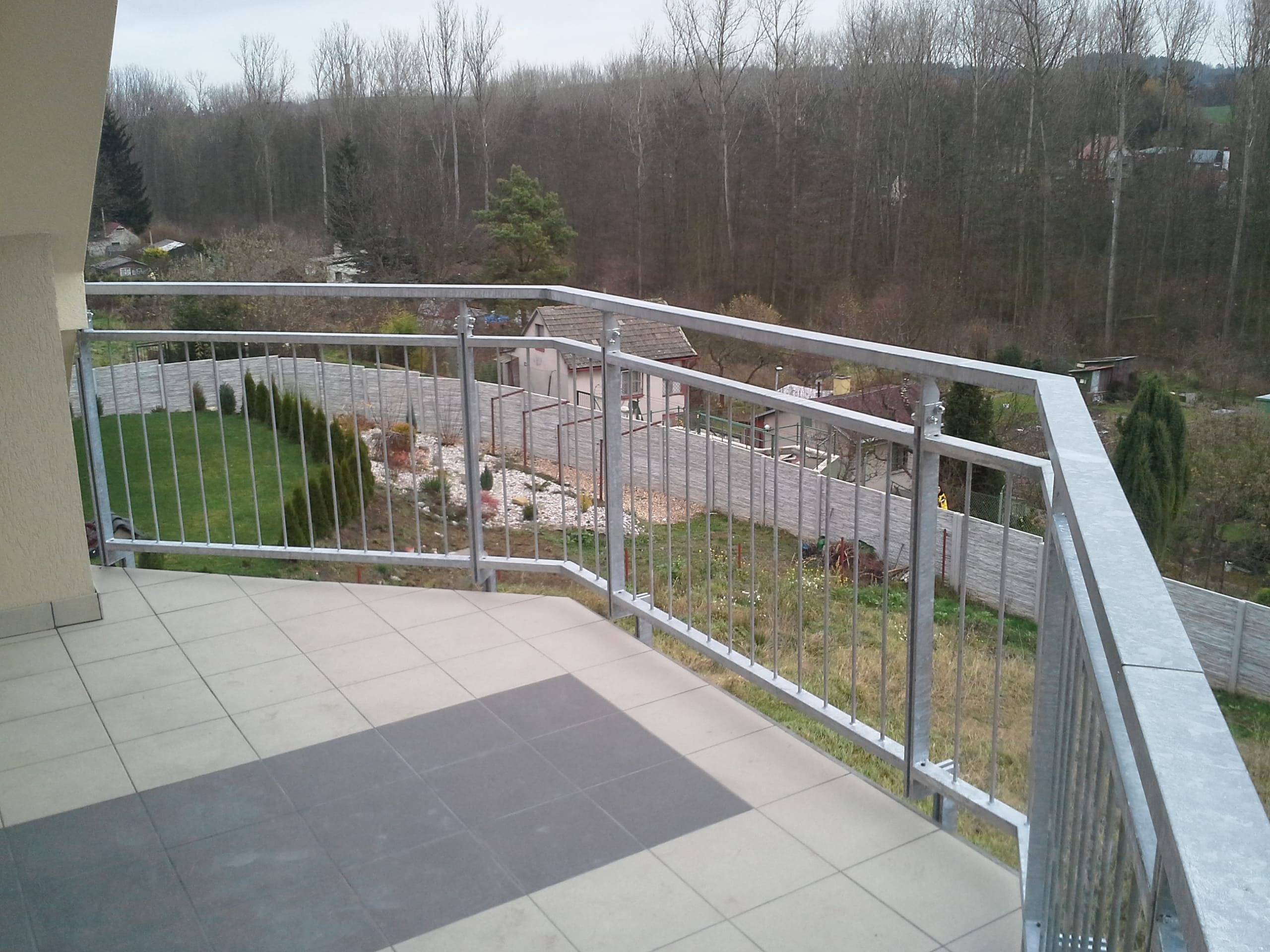 Žárově zinkované zábradlí se svislými tyčemi v rohu členitého balkónu ve Slaném.