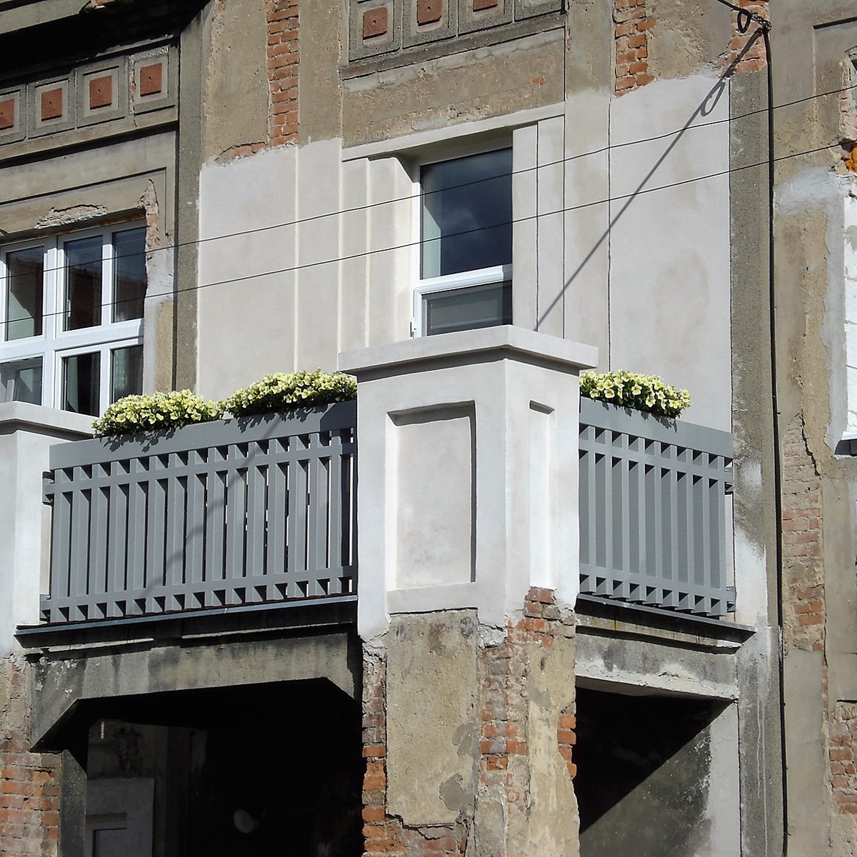 Celkový pohled zleva na balkon s šedým kovovým zábradlím navazujícím na zděné pilíře.