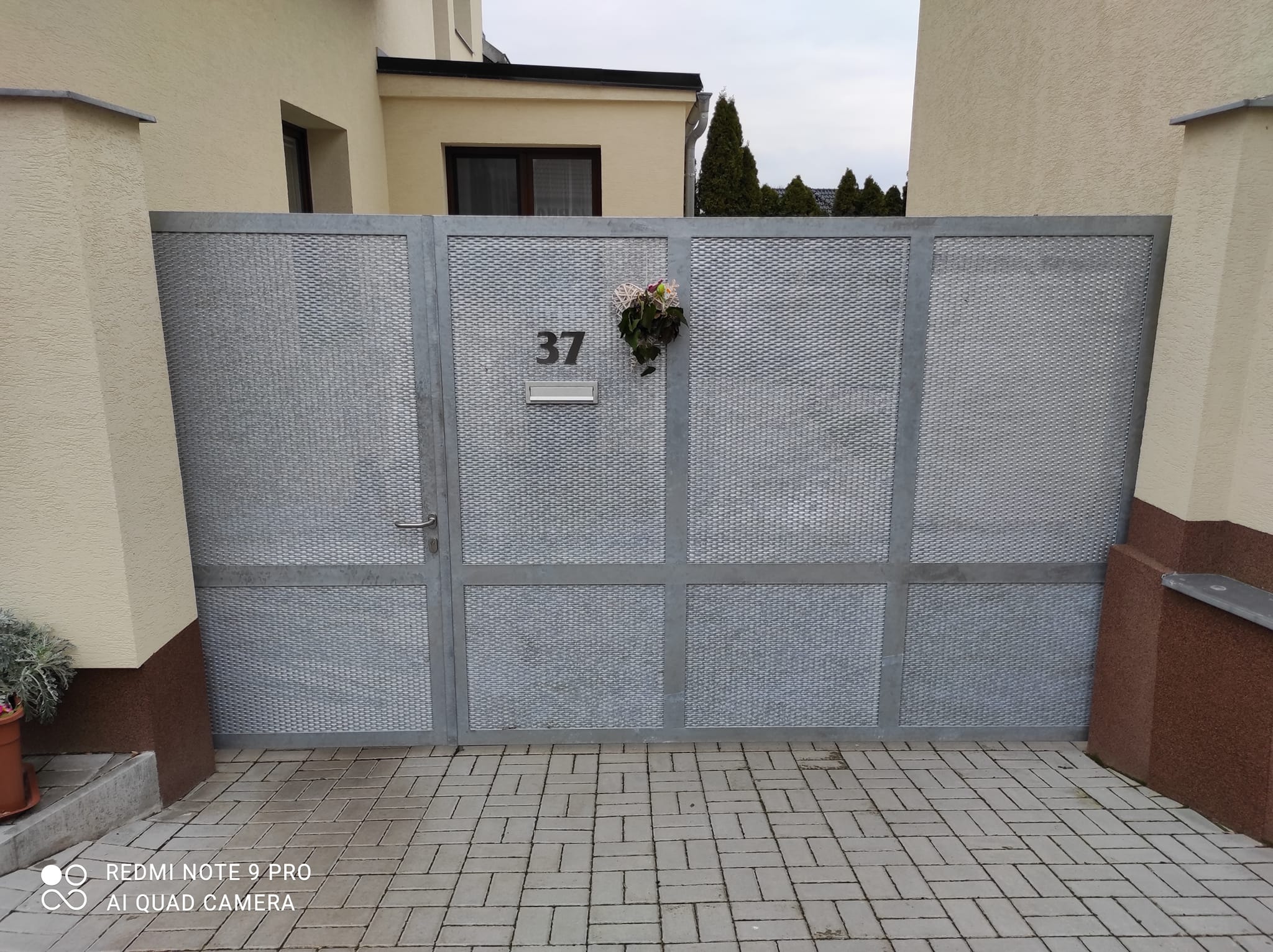 Čelní pohled na zinkovanou bránu a vstupní branku s tahokovem, klikou, poštovním vhozem a domovním číslem v Budeničkách.