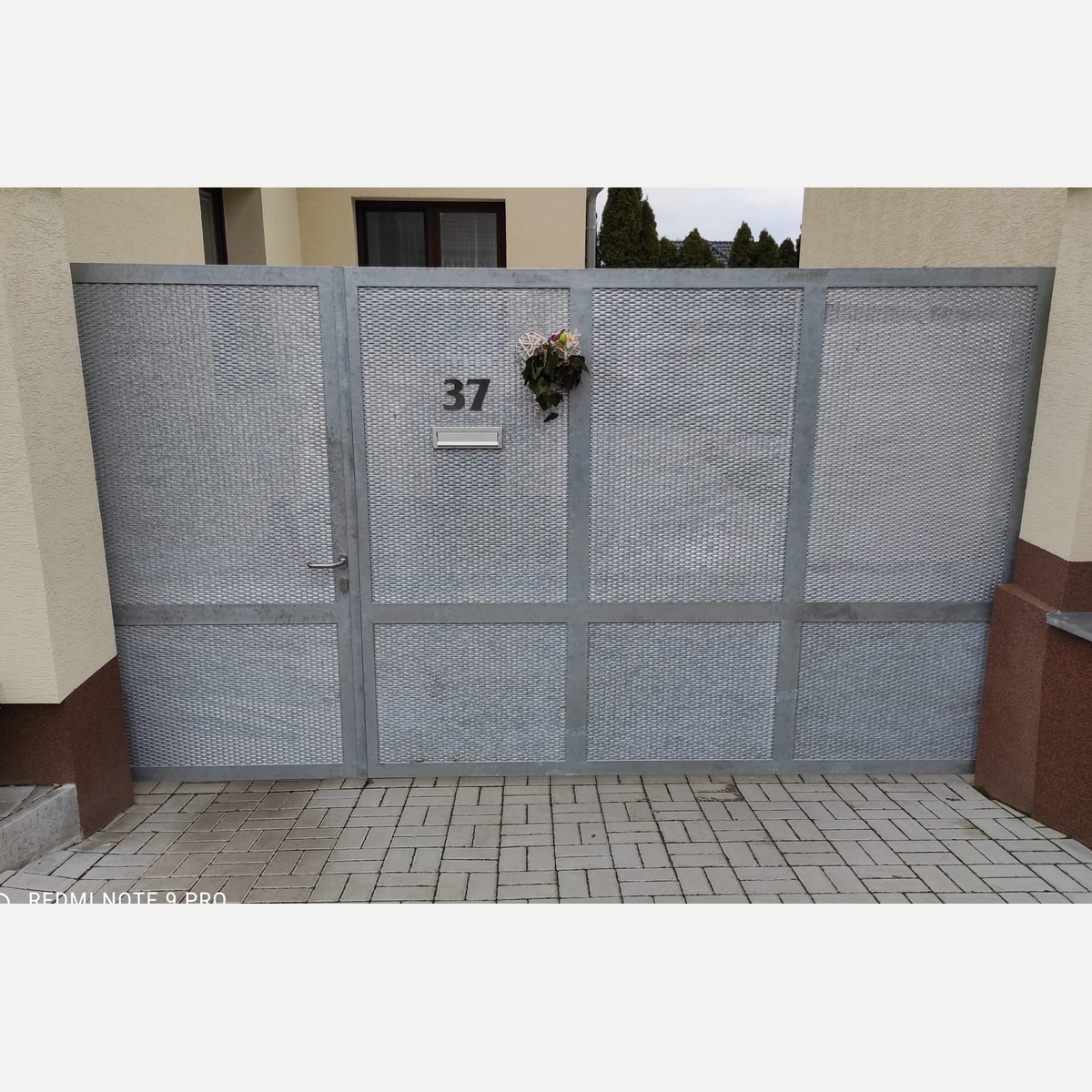 Čelní pohled na zinkovanou bránu a vstupní branku s tahokovem, klikou, poštovním vhozem a domovním číslem v Budeničkách.