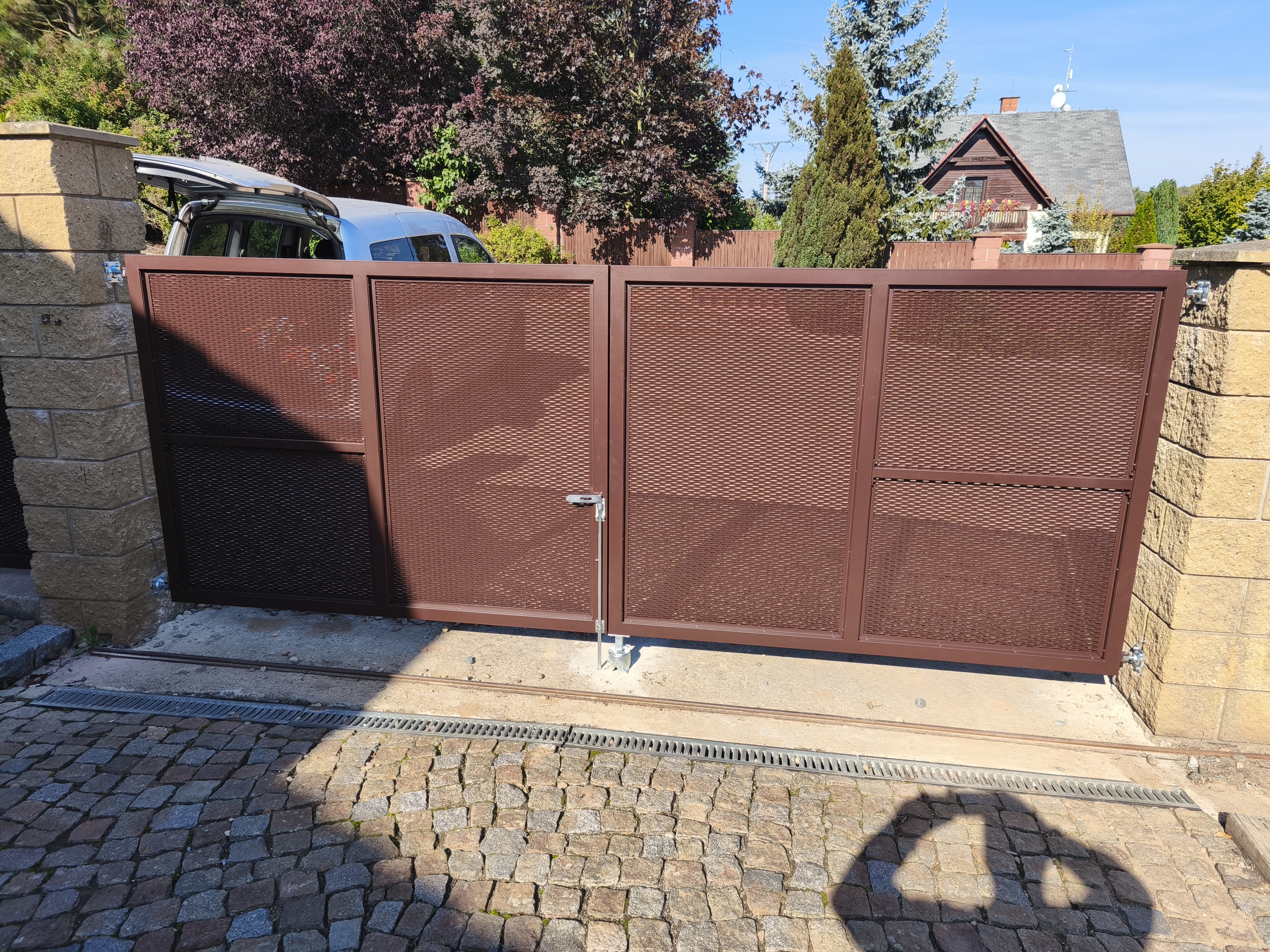 Čelní pohled z pozemku na novou dvoukřídlou bránu s hnědou tahokovovou výplní.