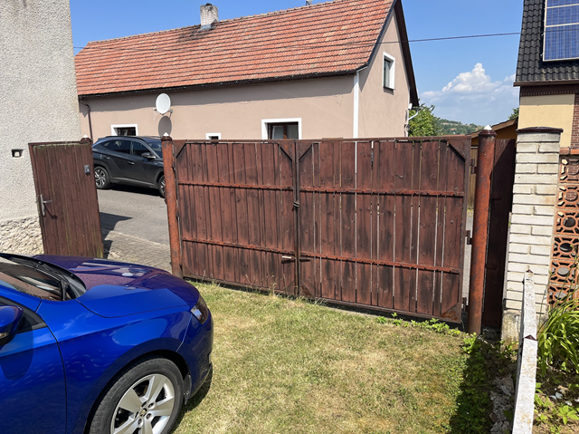 Vnitřní pohled na původní tmavou dřevěnou bránu a otevřenou branku před výměnou.