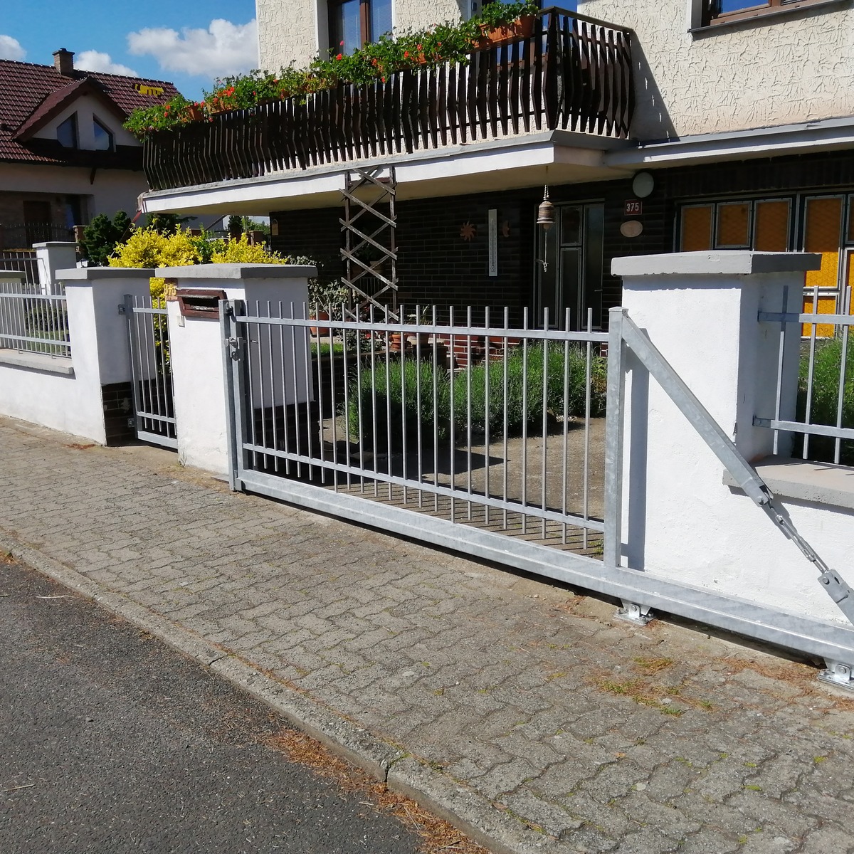 Detailní pohled z ulice na vjezdovou bránu, sousední branku a kovové výplně mezi zděnými sloupky.
