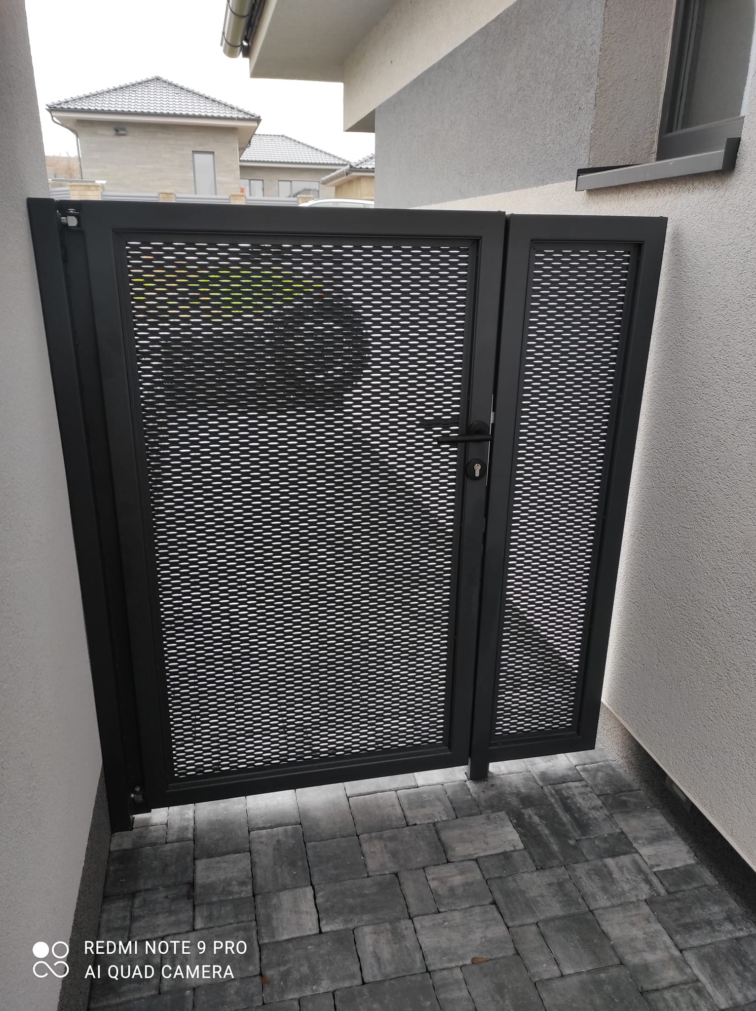 Pohled z opačné strany na dvoudílnou tahokovovou branku v průchodu mezi stěnami.