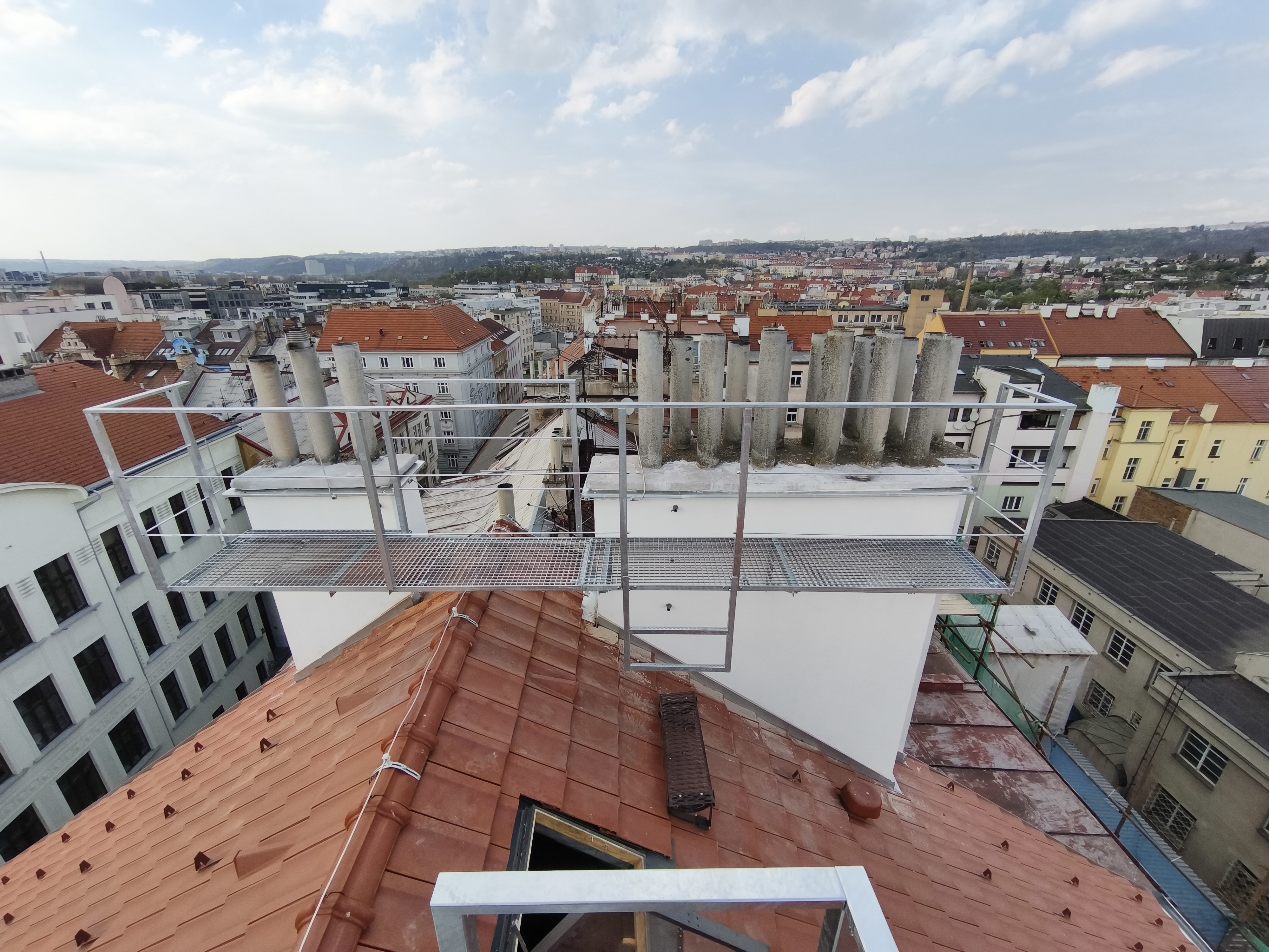 Celkový pohled na žárově zinkovanou lávku s roštovou podlahou a zábradlím před řadou komínových průduchů na Žižkově.