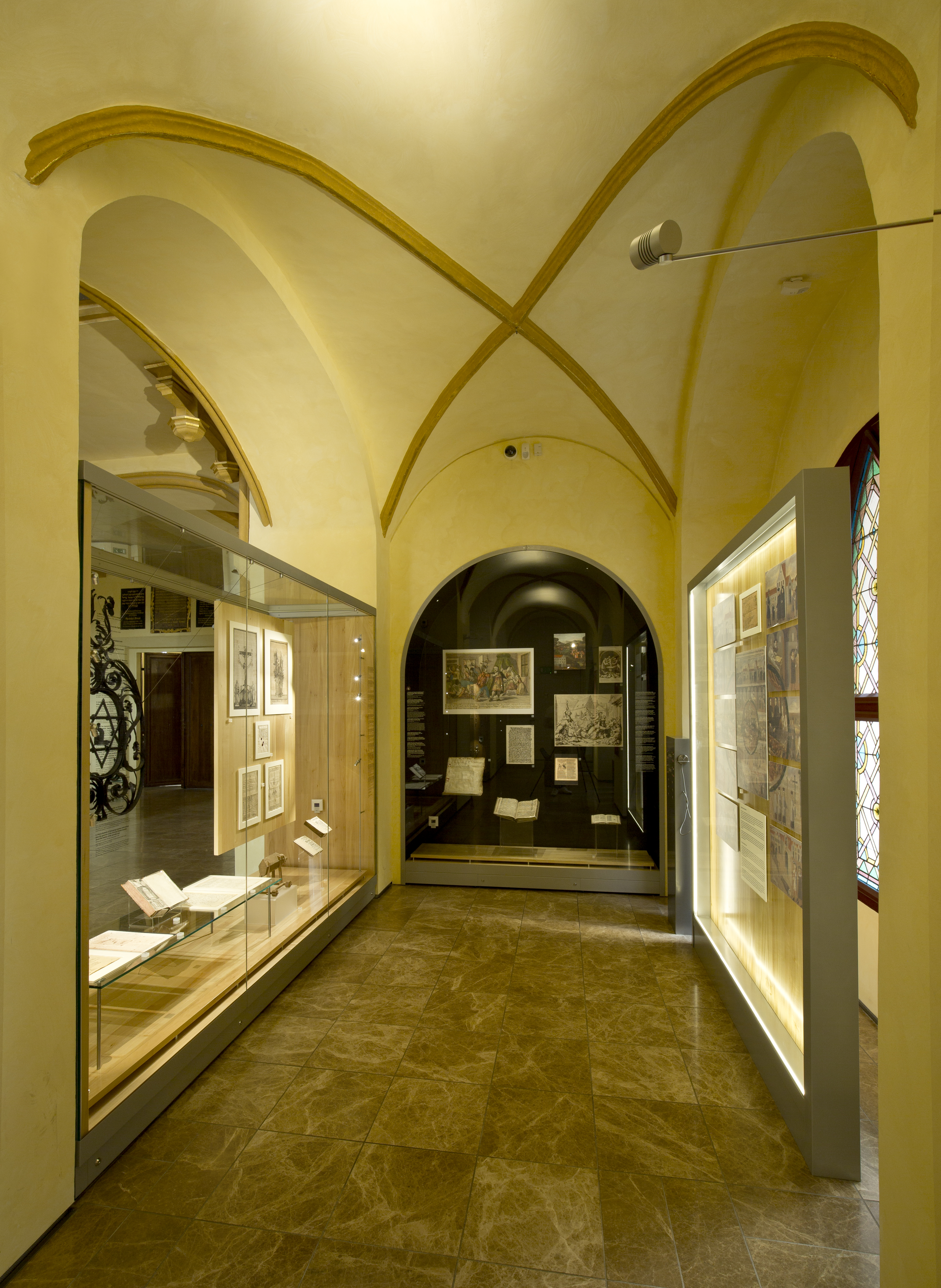 Pohled do výstavního prostoru Maiselovy synagogy s vitrínami osazenými na kovových soklech.