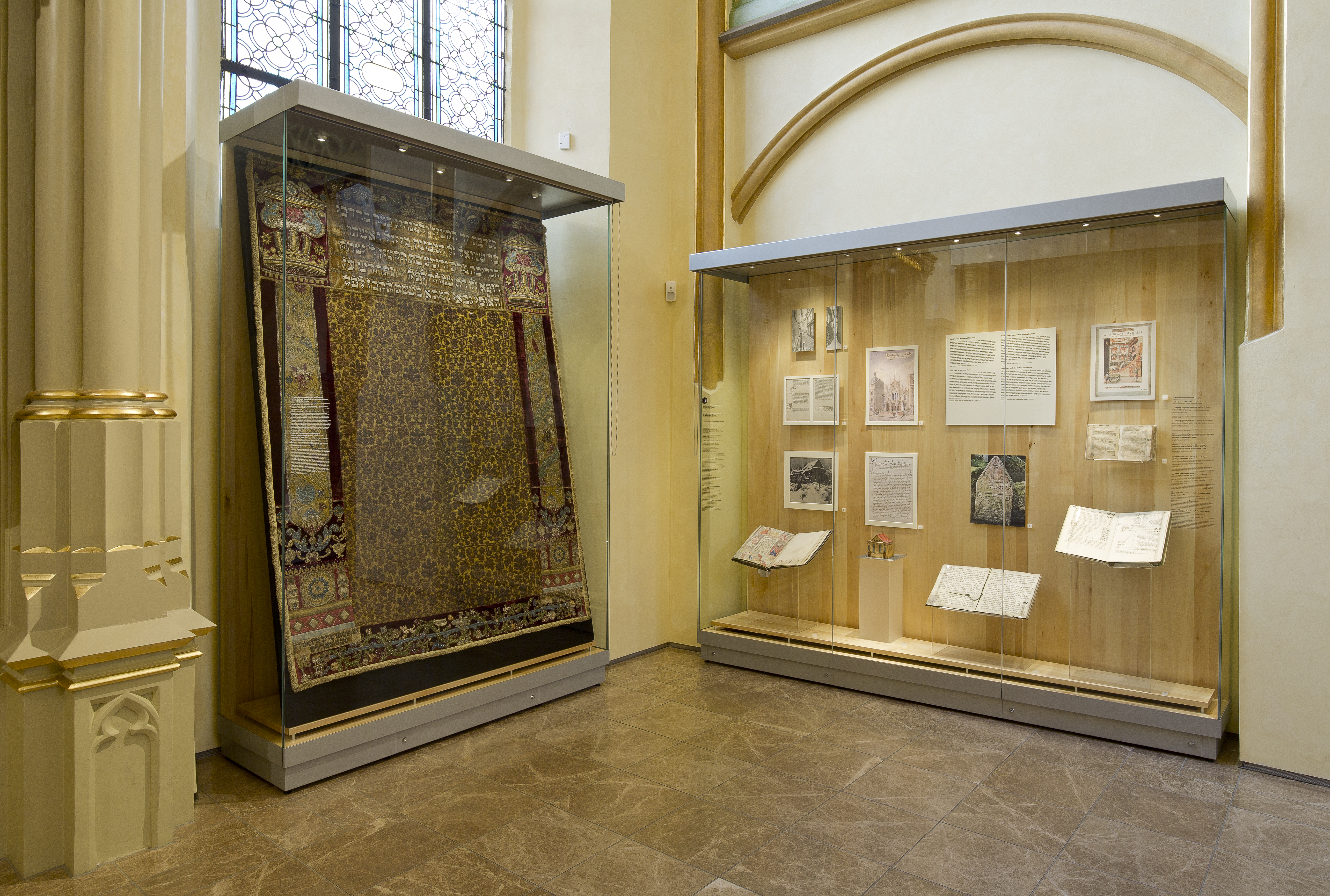 Výstavní vitríny v interiéru Maiselovy synagogy se stříbrnými kovovými sokly a konstrukčními prvky.