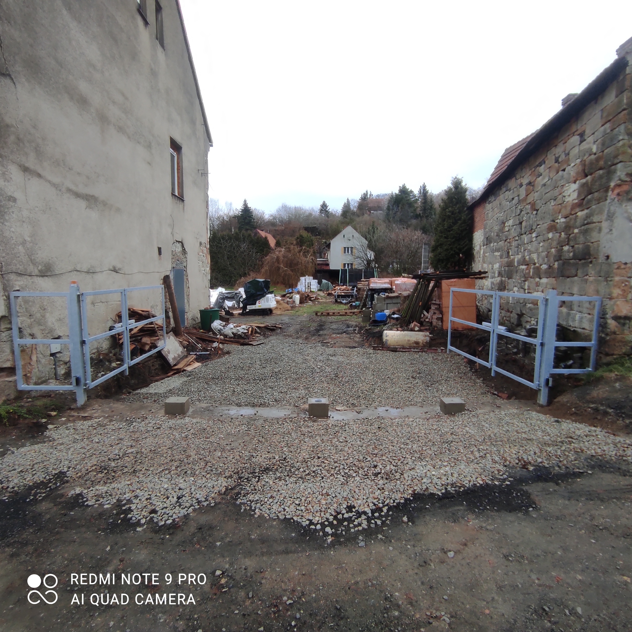 Pohled z ulice do otevřeného vjezdu v Bílichově s lomenými křídly složenými po stranách.