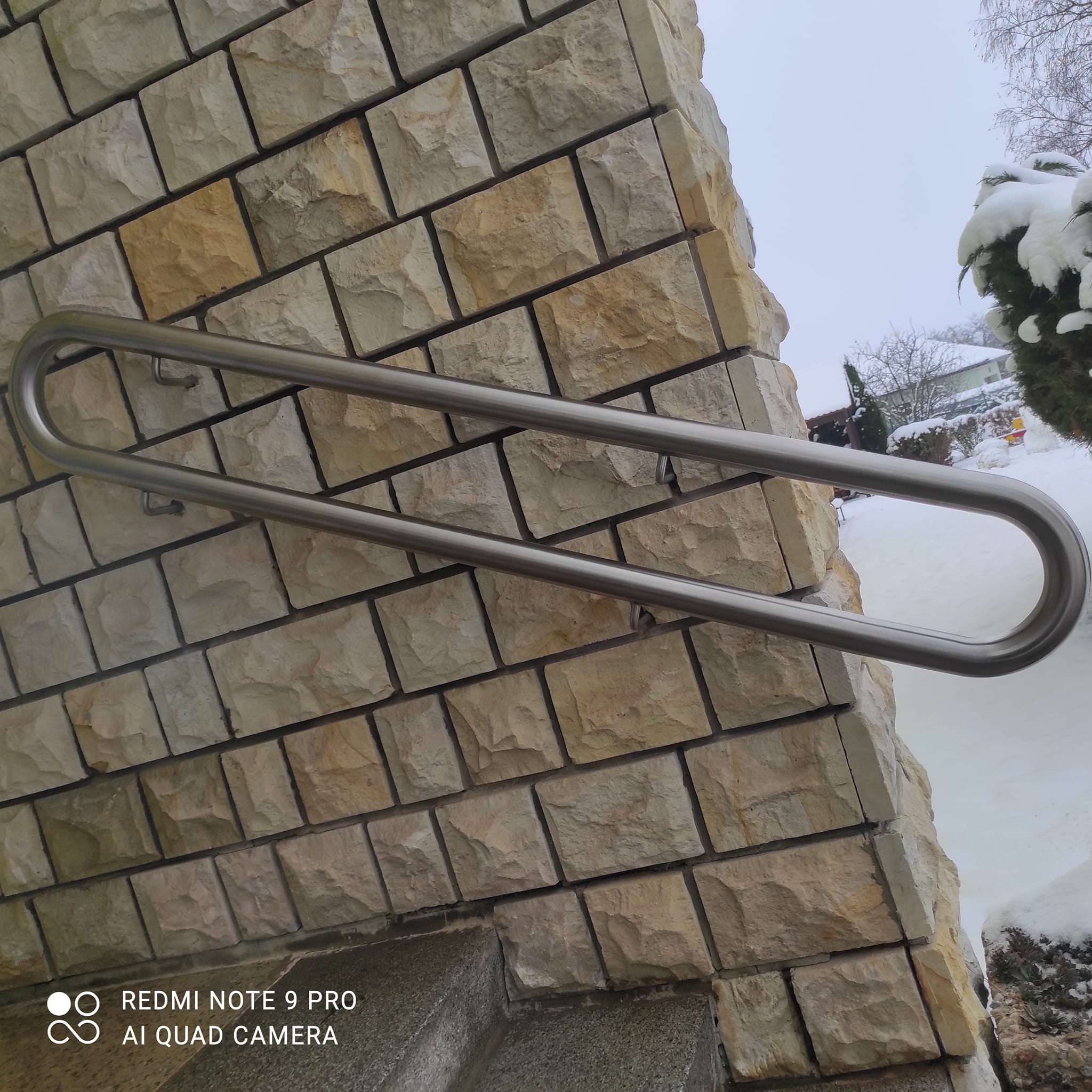 Detail zaobleného konce broušeného nerezového madla a konzol kotvených do obložené stěny.