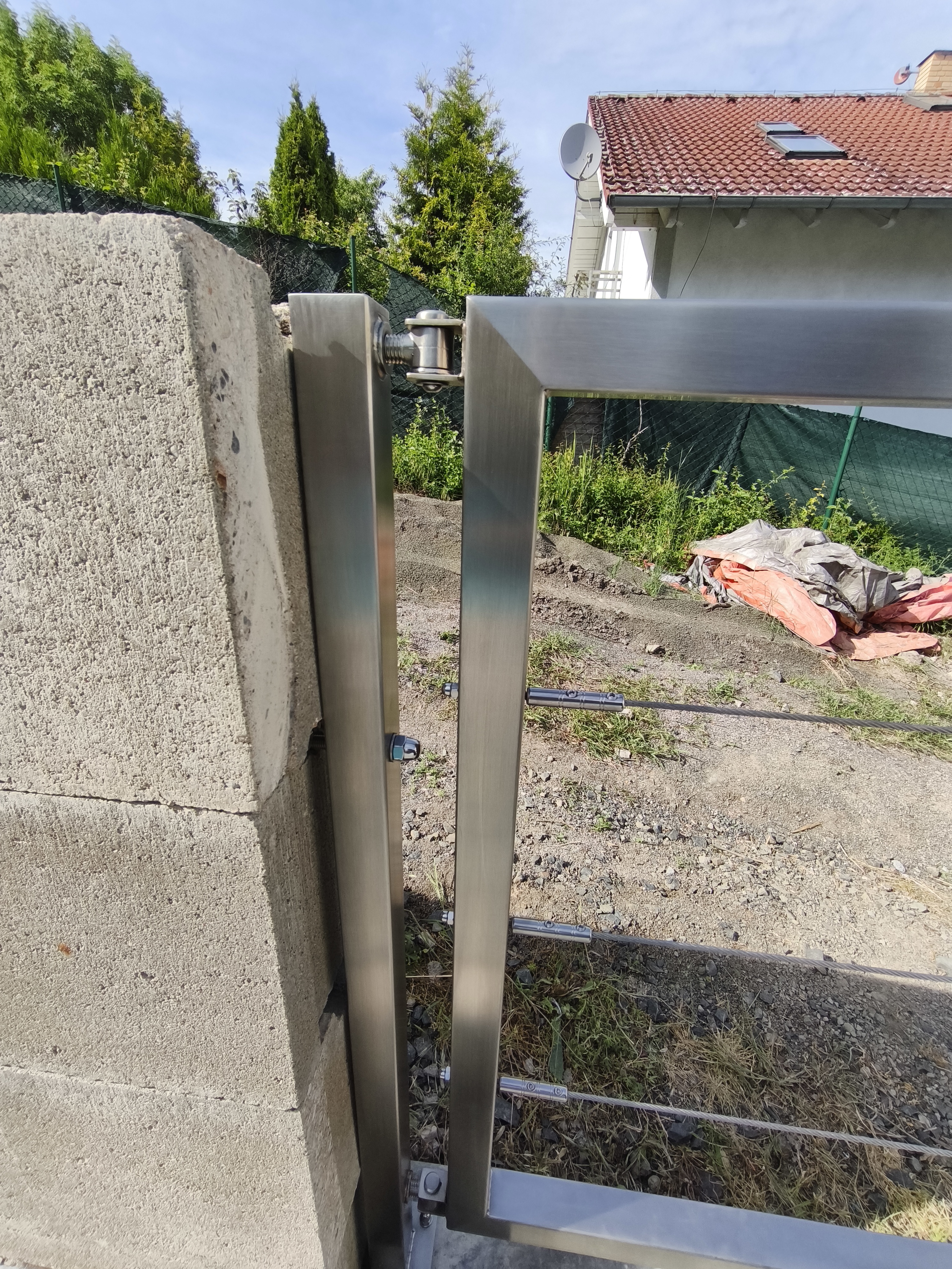 Bližší pohled na horní závěs, nerezový rám a lankovou výplň vstupní branky u bazénu.