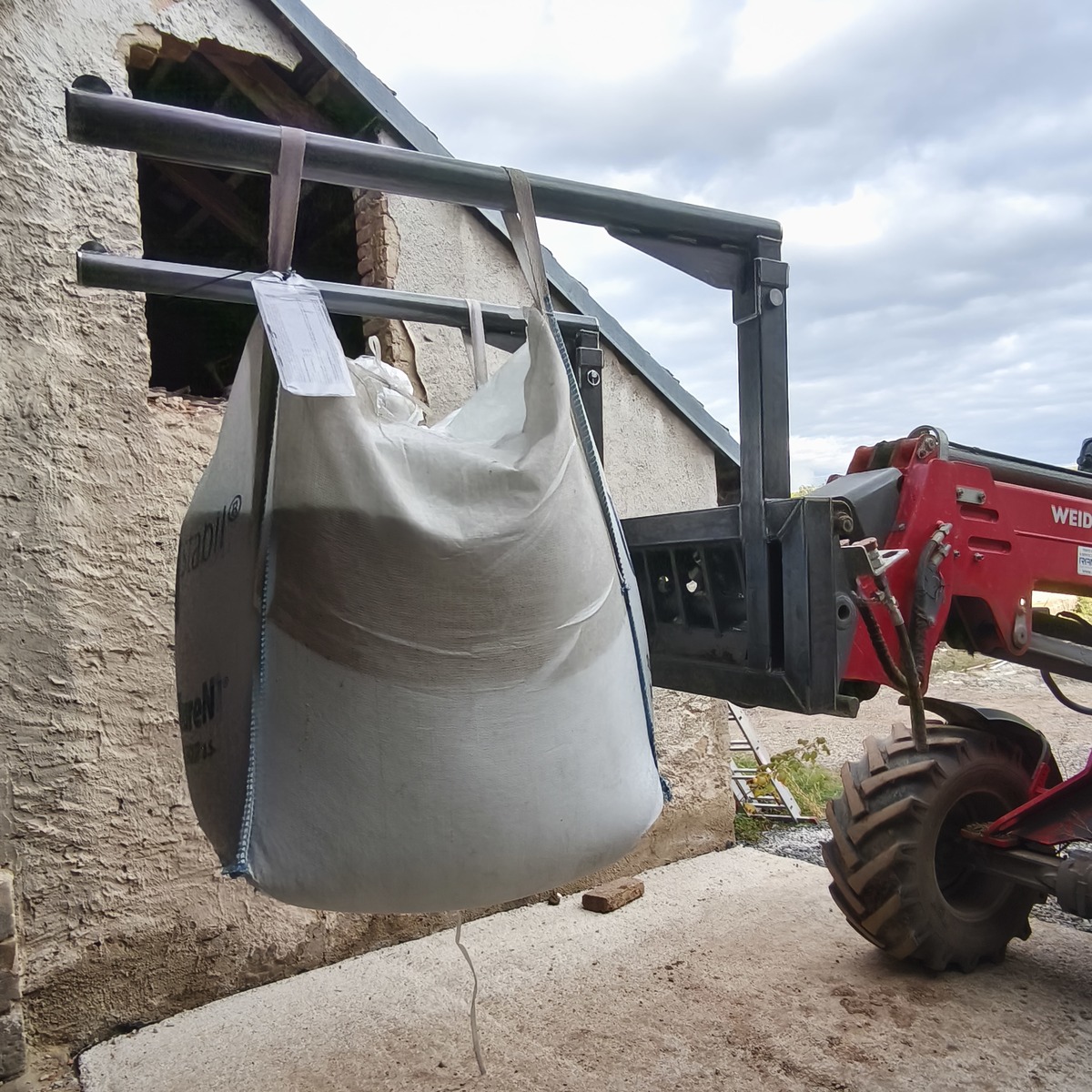 Boční pohled na svařovaný nosič a zavěšený Big Bag vak u manipulačního stroje venku.