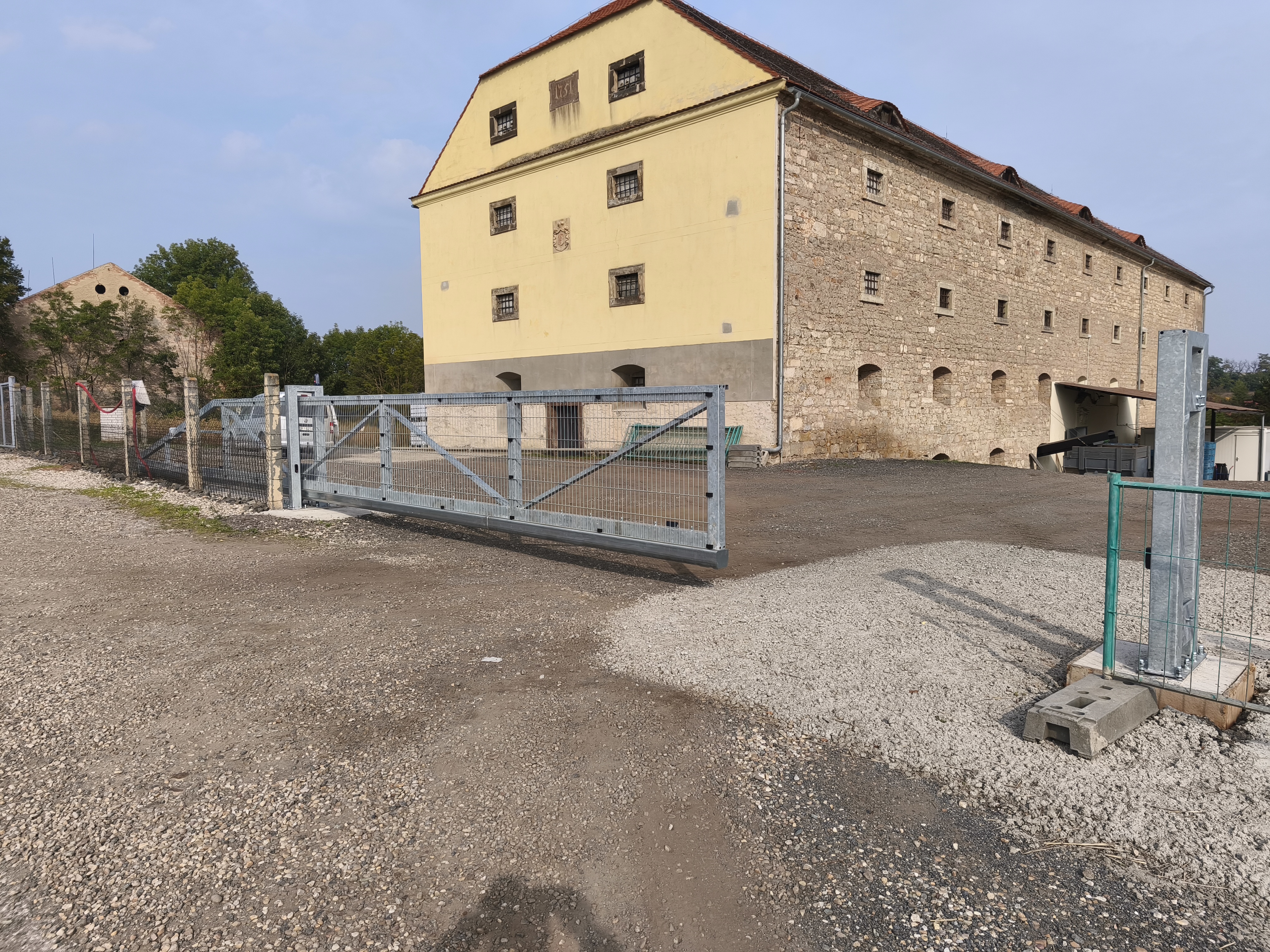 Samonosná brána odsunutá do strany s uvolněným vjezdem do areálu.