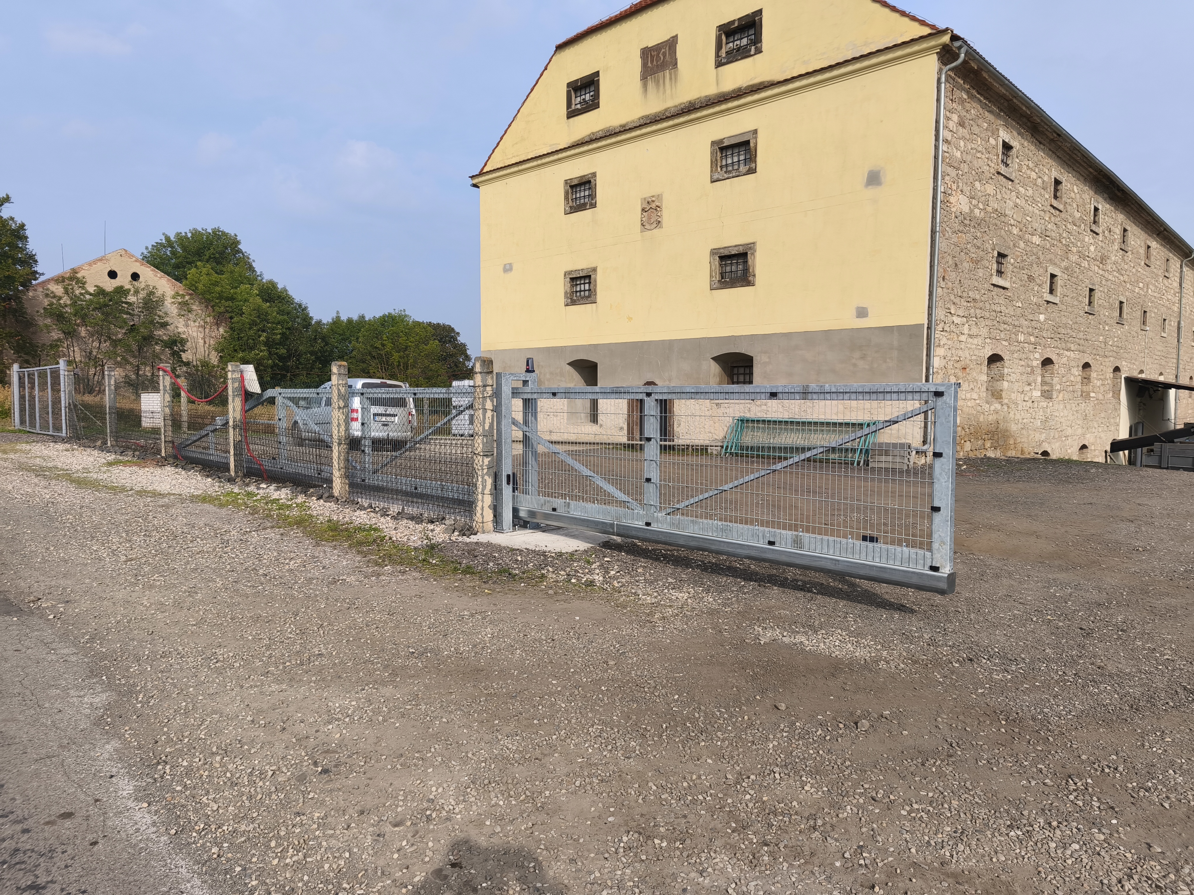 Zavřená pozinkovaná samonosná brána se svařovanými 2D panely před vjezdem do areálu.