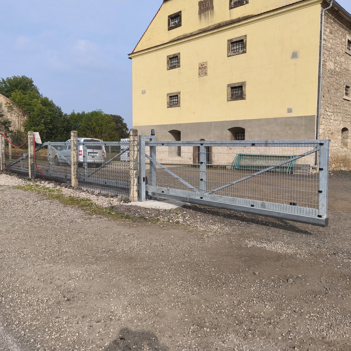 Zavřená pozinkovaná samonosná brána se svařovanými 2D panely před vjezdem do areálu.