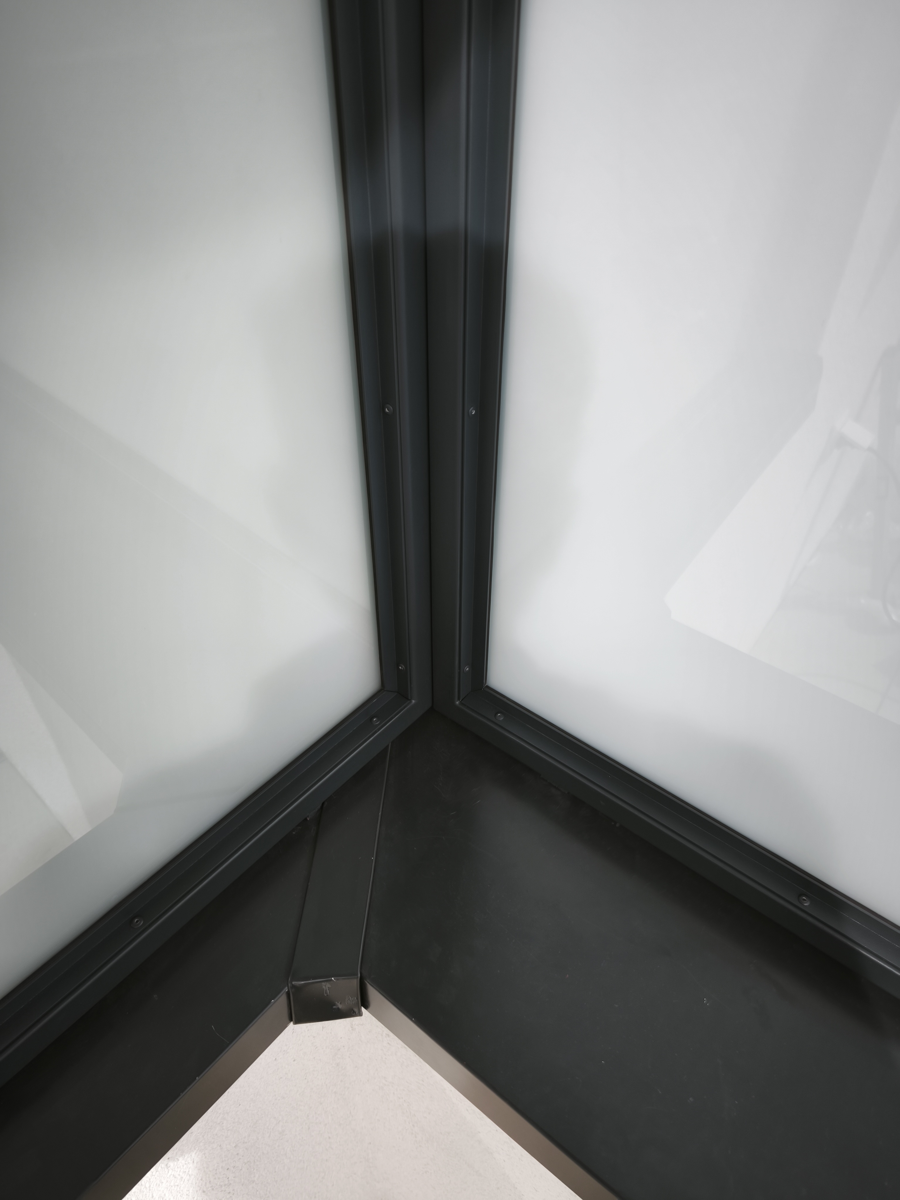 Detail spodního rohového spojení antracitových rámů prosklené zástěny.