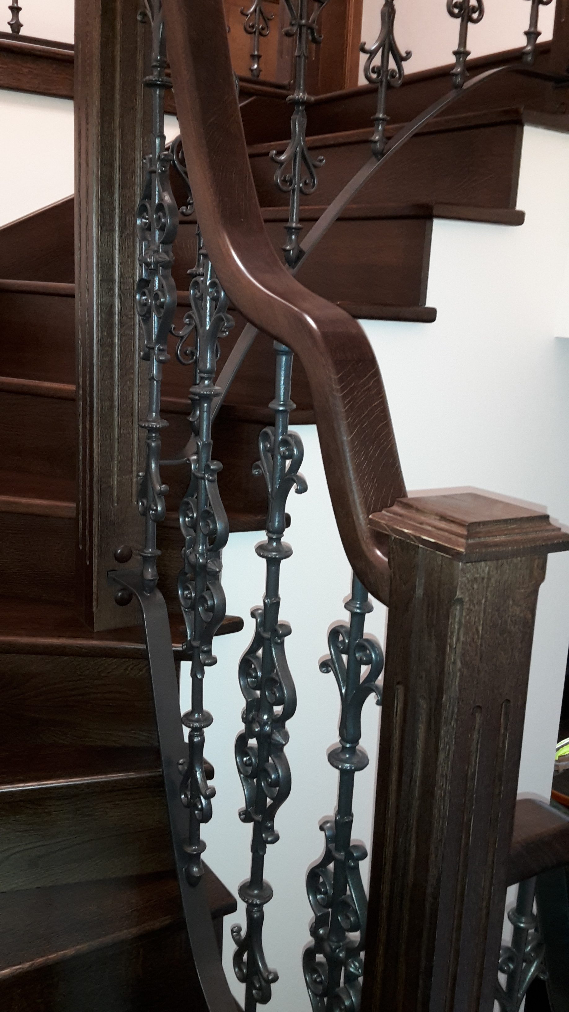 Detail zalomení a tvarování dřevěného madla u sloupku nad schodišťovými stupni.