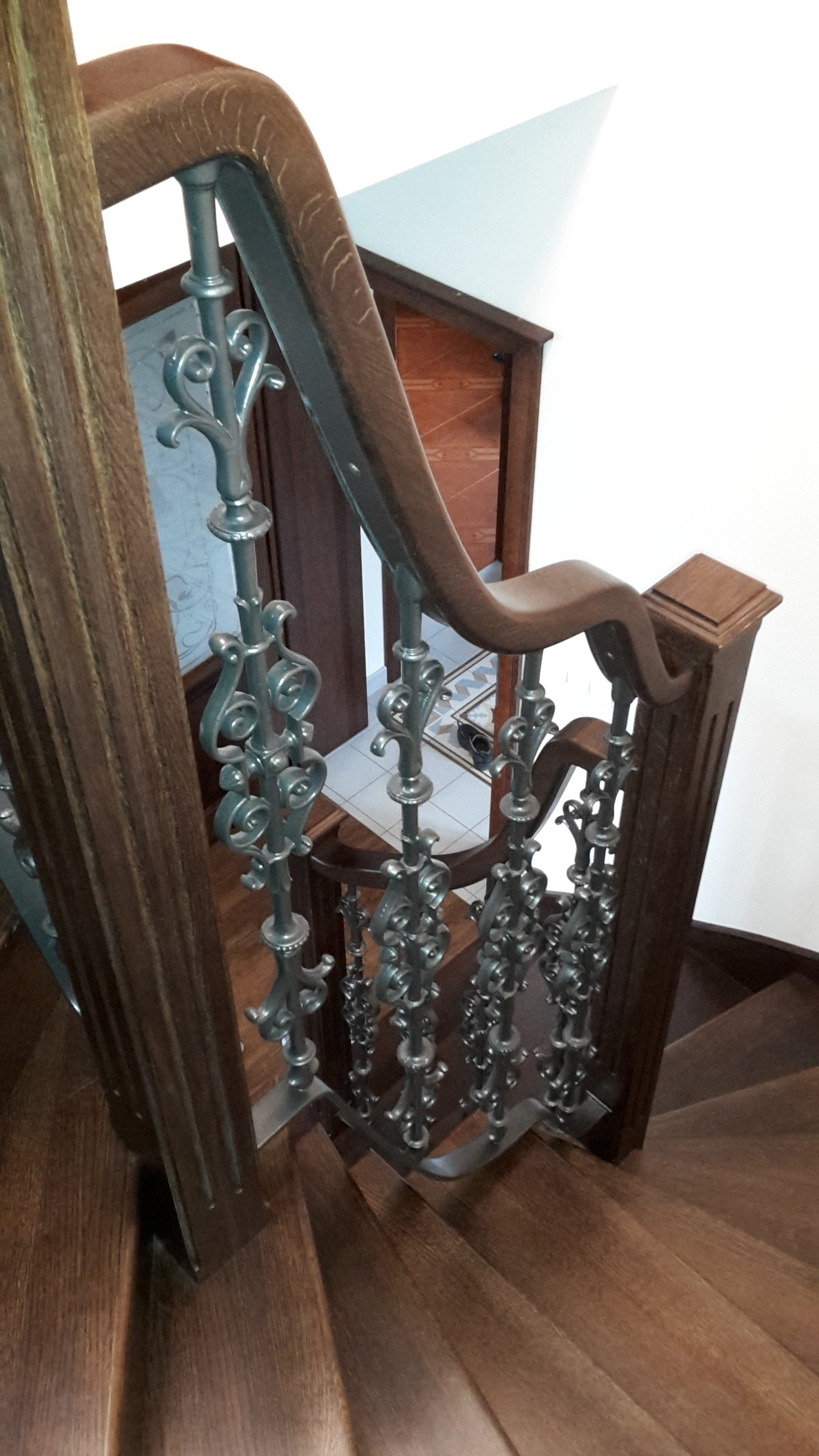 Detail tvarovaného dřevěného madla nad šikmým úsekem litinového zábradlí.