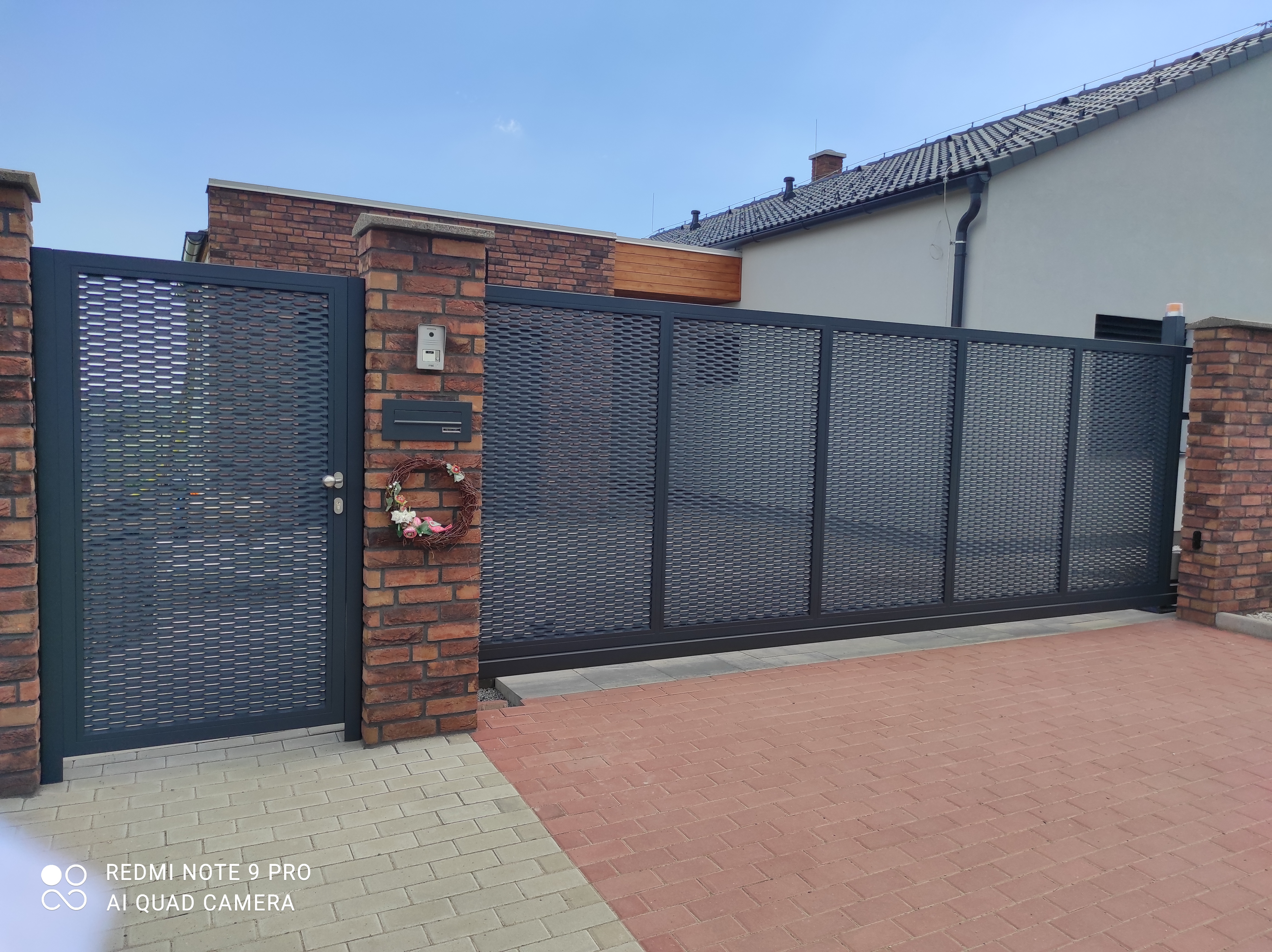 Celkový pohled z ulice na samonosnou bránu a vstupní branku s antracitovou tahokovovou výplní.