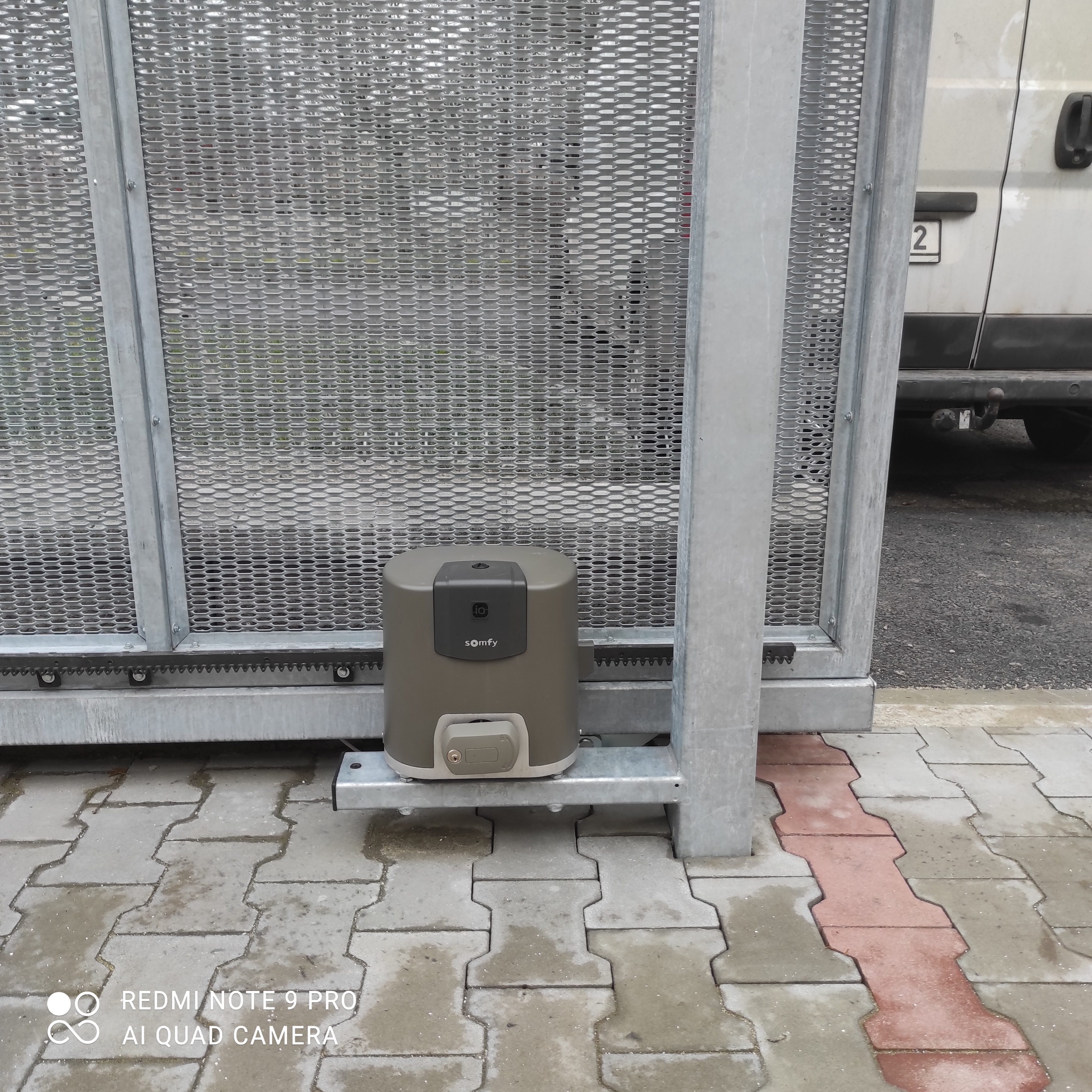 Motor pohonu Somfy u spodního profilu pozinkované samonosné brány s tahokovem.
