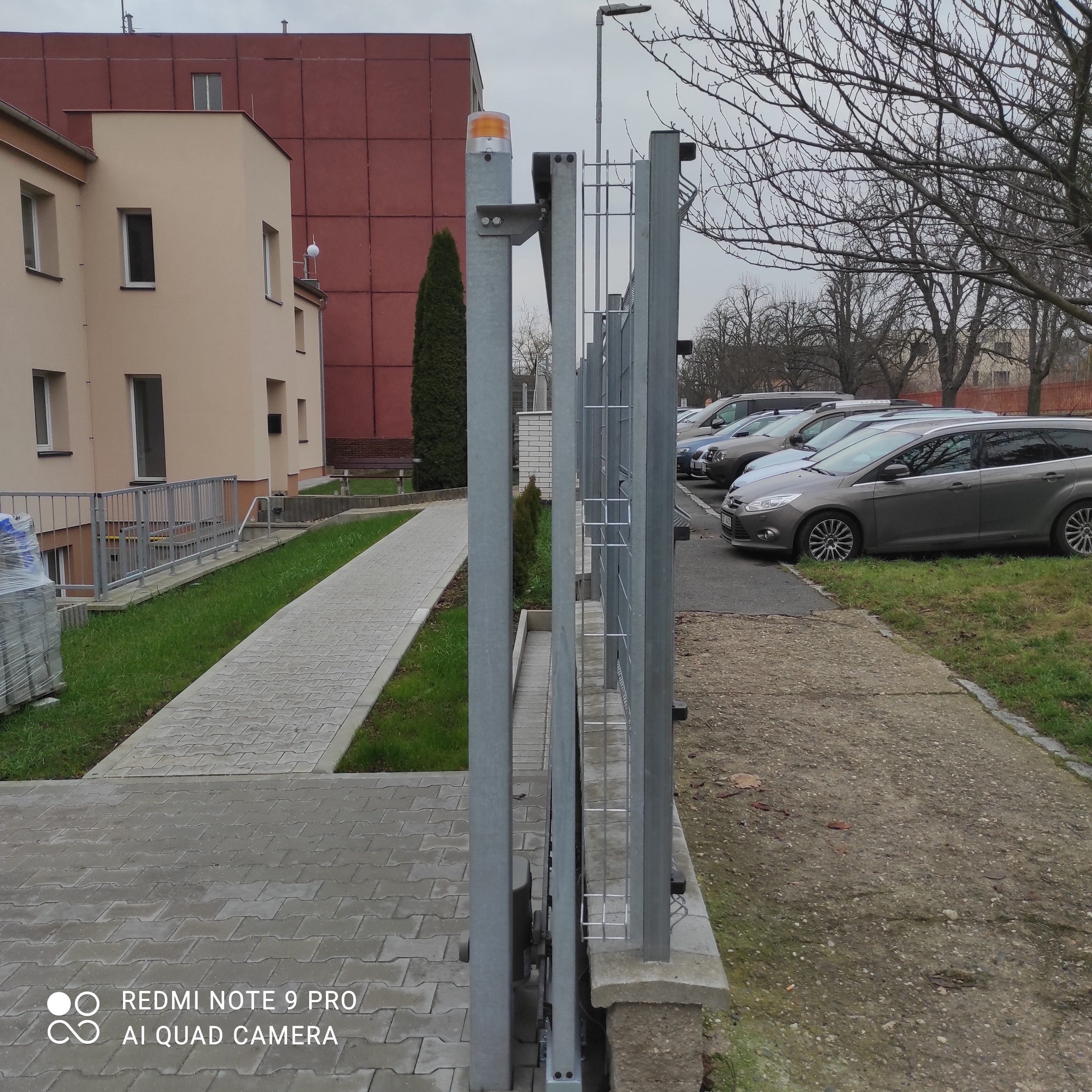 Čelní detail vedení a pozinkovaného sloupku samonosné brány podél oplocení.