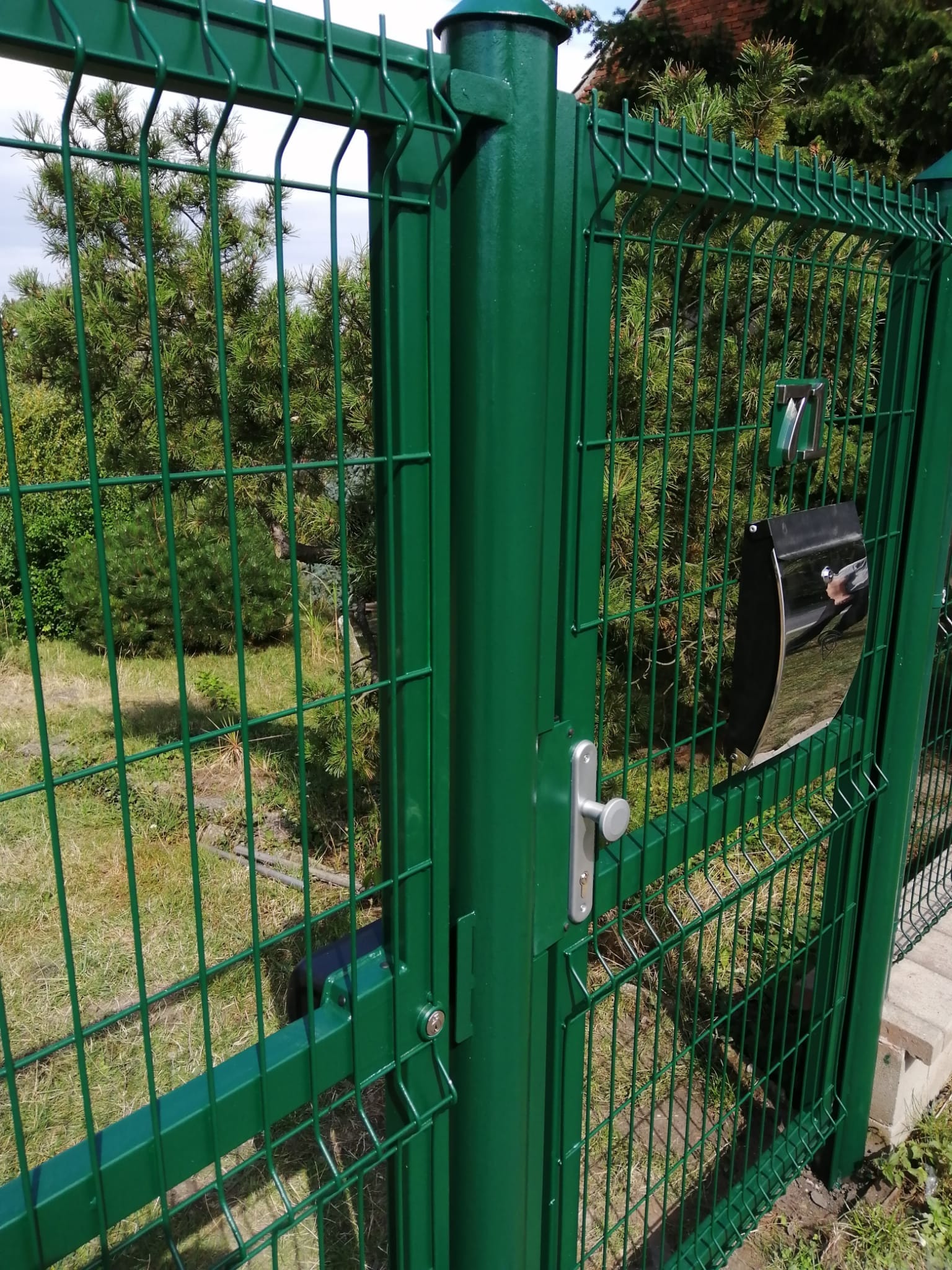 Detail kování zelené vstupní branky, jejího osazení u původního sloupku a výplně z 3D pletiva v Hvězdě.